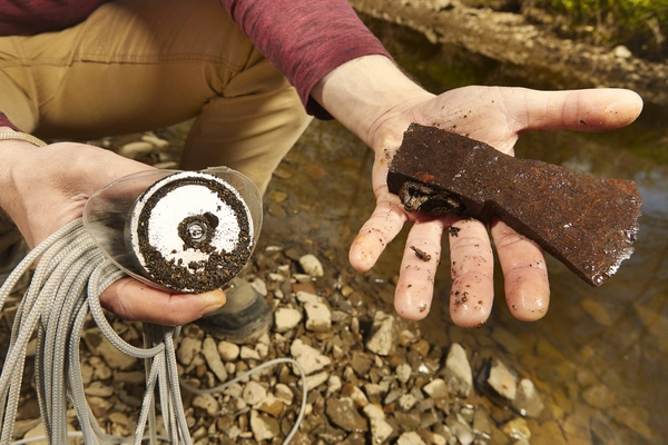 Ein mann hält eine alte Axt die er beim Magnetfischen aus dem Wasser gezogen hat