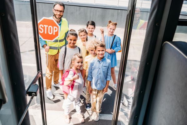 Kinder werden von einem Schülerlotsen zum Bus geführt