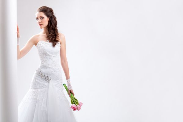 ein Braut im weißen Hochzeitskleid steht an einer Säule