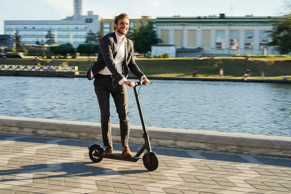 Wie funktioniert das Ausleihen von E-Scootern? Junger Geschäftsmann fährt E-Scooter in der Stadt.
