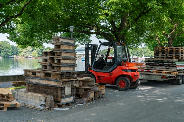 Roter Gabelstapler fährt Baustellengut vom Straßenrand weg.